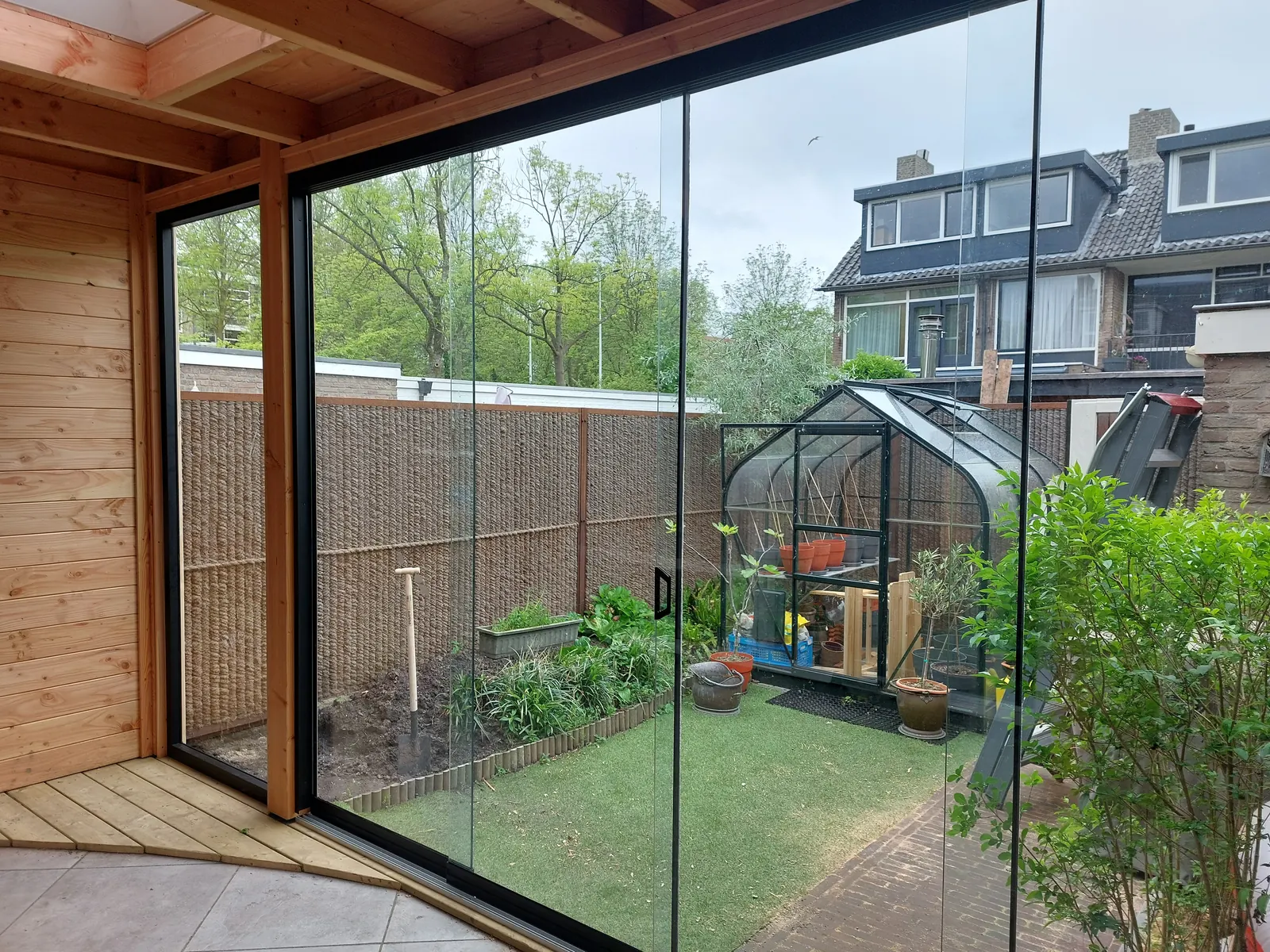 Uitzicht vanuit een houten overkapping door glazen schuifwanden op de tuin